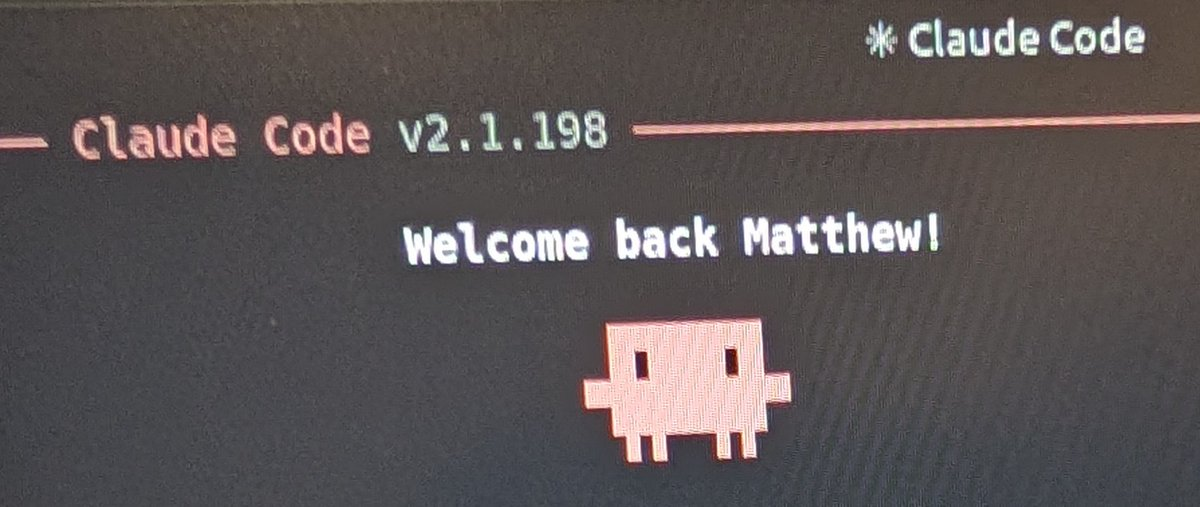 A close photo of a monitor showing the Claude Code terminal splash screen — the version banner and a greeting line, with the small pixel-art mascot underneath
